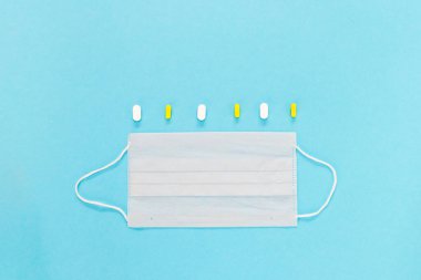 Beyaz tıbbi koruyucu maske, haplar ve mavi arka planda termometre. Coronovirus önleme ve sağlık hizmeti kavramı. yatay görünüm telif uzayı