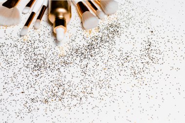Makyaj fırçaları, hiyalürik asit ve beyaz arka planda altın parıltılı konfeti. yatay görünüm telif uzayı.