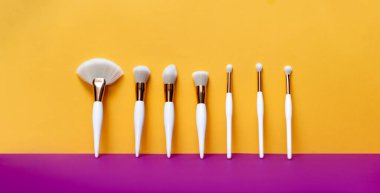 Makyaj düz fırçalar sarı ve mor arkaplan. Yatay üst görünüm telif uzayı. Güzellik ve makyaj