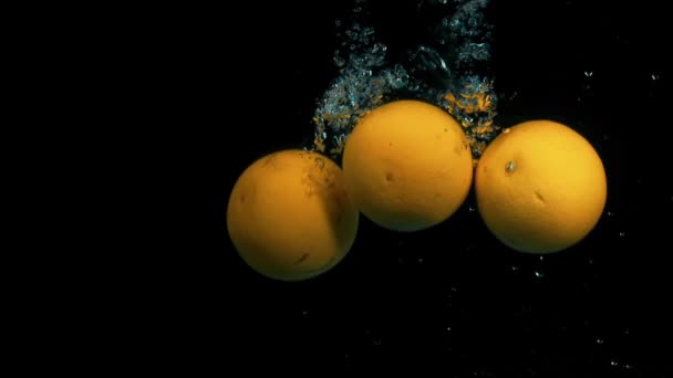 Sinaasappels vallen in water in slowmotion op zwarte achtergrond — Stockvideo