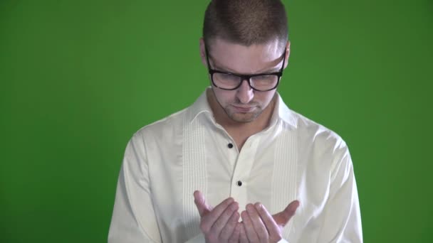 Een getextureerd man met een stoppels en glazen onderzoekt zijn handpalmen op een groene achtergrond — Stockvideo