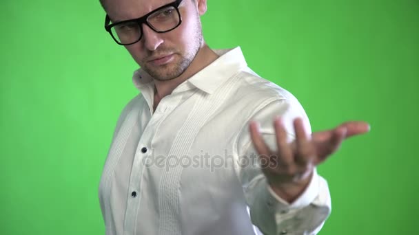 Een getextureerd man met een stoppels en glazen onderzoekt zijn handpalmen op een groene achtergrond — Stockvideo