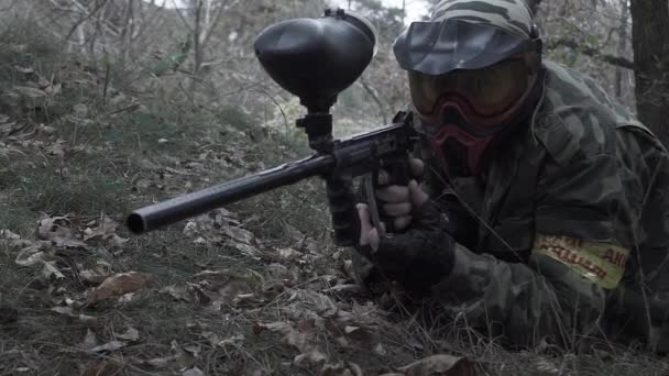 A man lying on the grass shooting from a paintball in slow motion — Stock Video