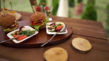 Hamburger ve Salatalar plakaları, sergilenen doğada ahşap bir masa üzerinde.