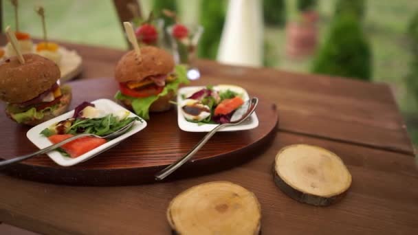 Hamburgers et salades sur assiettes, exposés sur une table en bois dans la nature . — Video