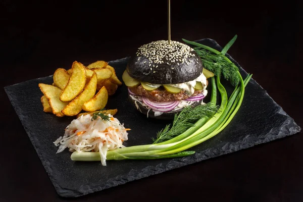 Hamburguesa negra con cebolla y pepinos sobre mesa de piedra con fondo negro . — Foto de Stock