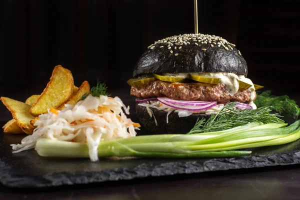 Soğan ve salatalık taş tablo siyah arka plan üzerinde siyah hamburger.
