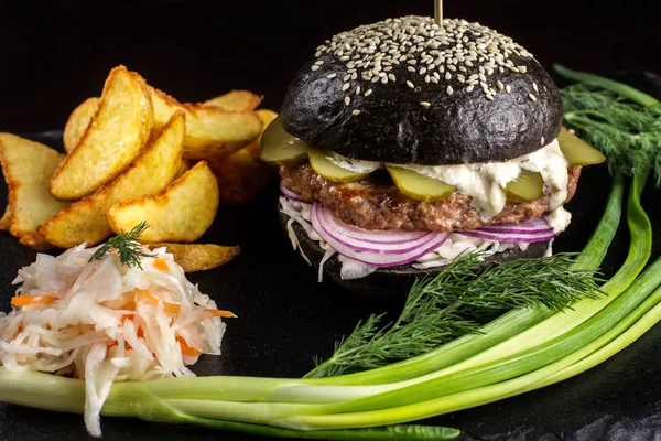 Hamburguesa negra con cebolla y pepinos sobre mesa de piedra con fondo negro . — Foto de Stock