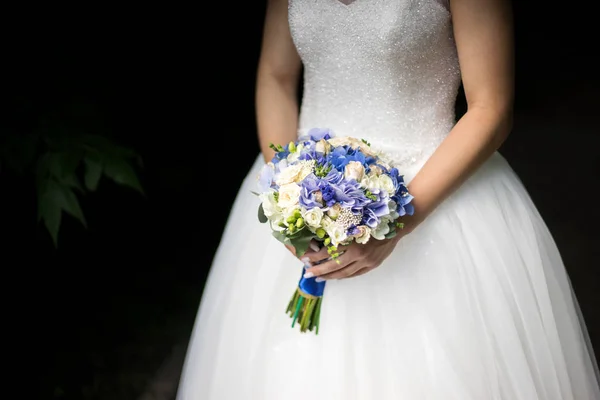 Наречена в сукні стоїть в зеленому саду і тримає весільний букет з квітів і зелені . — стокове фото