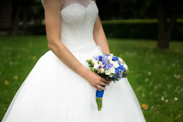 Νύφη σε ένα φόρεμα που στέκεται σε ένα καταπράσινο κήπο και κρατώντας μια γαμήλια ανθοδέσμη από λουλούδια και την πρασινάδα-2 — Φωτογραφία Αρχείου