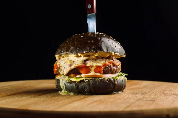 Primer plano de deliciosa hamburguesa de carne fresca hecha en casa con lechuga, queso, cebolla y tomate. Cuelga una esquina de queso. Bollo negro . — Foto de Stock