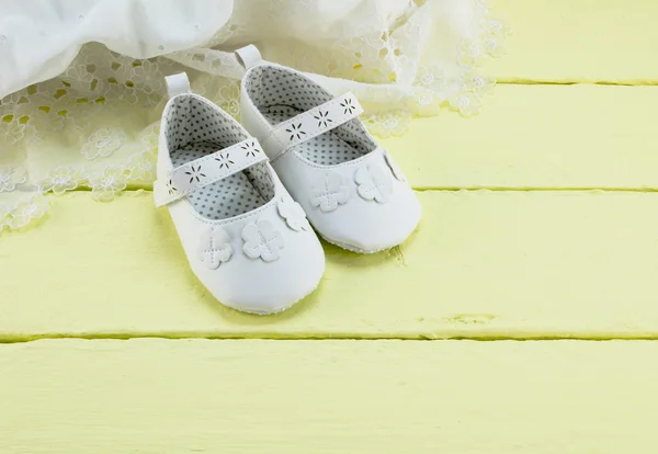 Baby white booties on yellow wood background with white lace dre — Stock fotografie