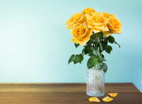 在木桌上有一个玻璃花瓶中的黄玫瑰 — 图库照片