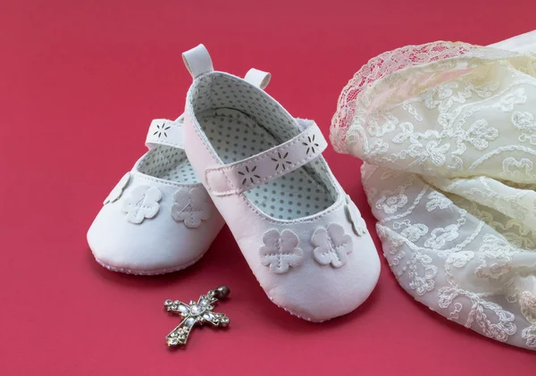 Pair of white baby booties on red background with vintage lace christening dress — Stock Photo, Image