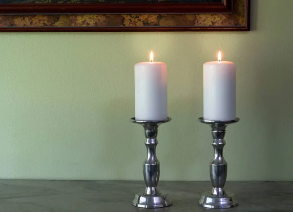 Dos velas blancas encendidas en canelabra contra la pared verde textura ba — Foto de Stock