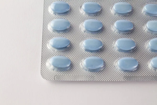Синие овальные таблетки в блистерной упаковке на белом крупным планом — стоковое фото