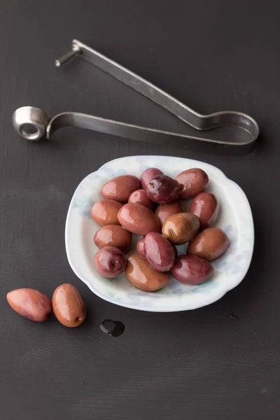 Olive viola in piccola ciotola bianca con due su tavola di gesso nero — Foto Stock