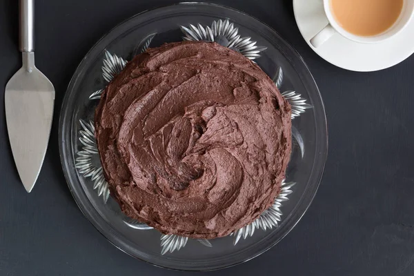 Choclolate cake on glass plate with silver server and cup of tea — Stock Photo, Image