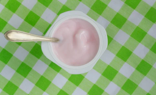 Tazza di yogurt con yogurt alla fragola rosa su geen e tavolo bianco — Foto Stock