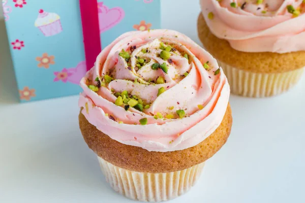 Two peach rose swirled frosted cup cakes with pistachio nut spri