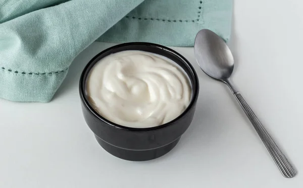 Yogur cremoso en tazón de cerámica negra con cuchara de metal sobre ba blanca —  Fotos de Stock