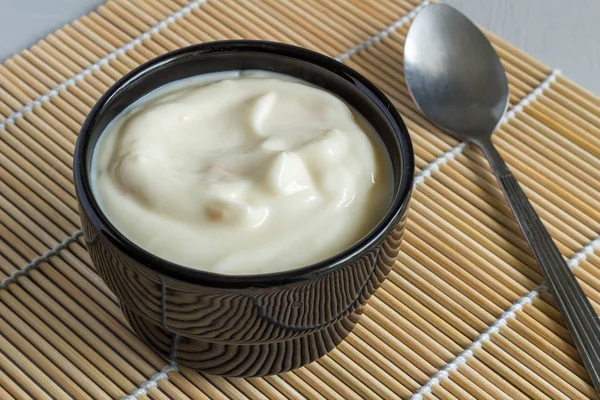 Yogur de fruta cremoso en un tazón negro en una alfombra de mesa de caña de cerca —  Fotos de Stock