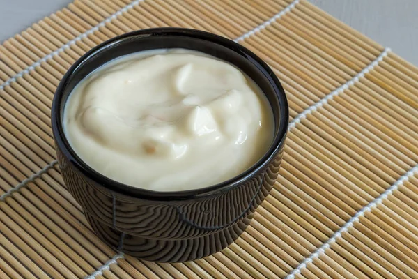 Yogur de fruta cremoso en un tazón negro en una alfombra de mesa de caña de cerca —  Fotos de Stock