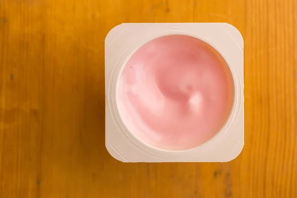 Yogurt alla fragola rosa in tazzina di plastica isolata su tavolo di legno — Foto Stock