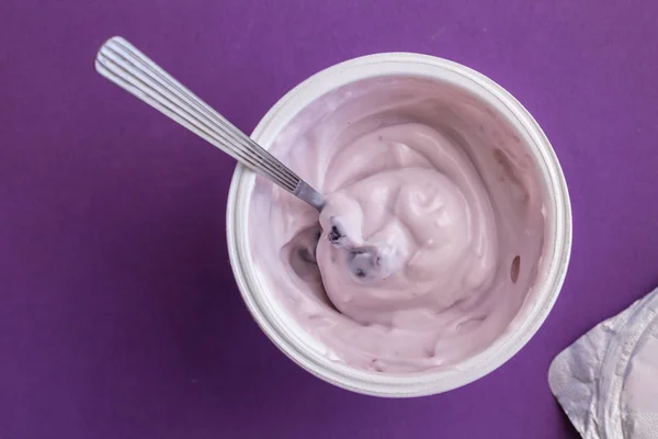 Blueberry yogurt with spoon in plastic cup with foil lid on side — Stock Photo, Image