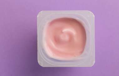 Sağlıklı çilek aromalı yoğurt, mor arka planda izole edilmiş küçük plastik bardakta doğal renklendirilmiş.