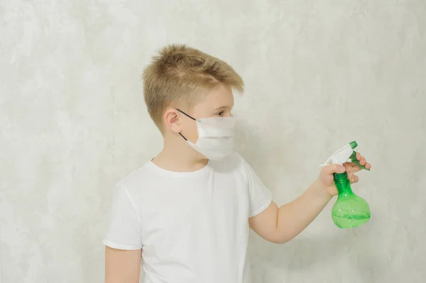 The boy in a protective medical mask sprays a disinfectant or antibacterial spray to prevent the spread of viruses and germs. Quarantine concept. Covid-19