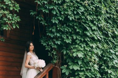 Bir gelinlik gelin portresi ile bir buket çiçek yeşil ile büyümüş bir ahşap evin girişinde.