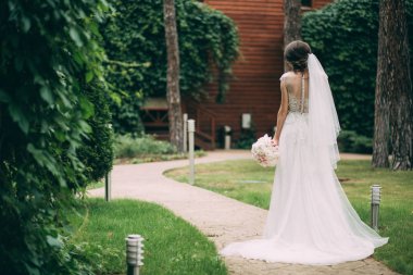 Gelin gelinlik sırtında bir buket ile doğa sokakta elinde duruyor.