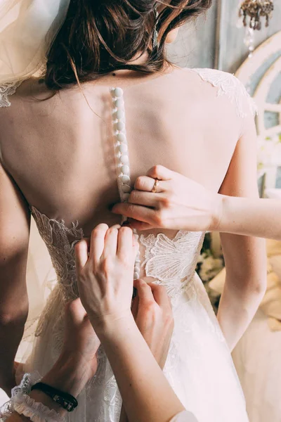 Hands of two girls who button up the buttons at the back of the wedding dress of the bride, Dressing up a bridal wedding dress, bridesmaids dressing a dress