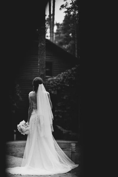 新娘站在她的婚纱礼服与她的手上的花束在大自然的小巷 — 图库照片