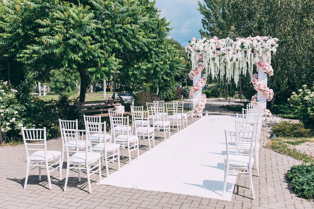 Wedding arch decorated with flowers. Chairs for guests. White track.
