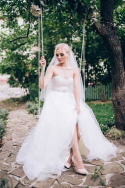 Gelin bir salıncak üzerinde beyaz elbiseli.