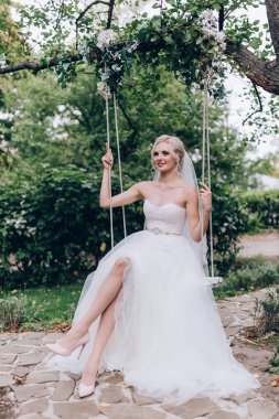 Gelin bir salıncak üzerinde beyaz elbiseli.