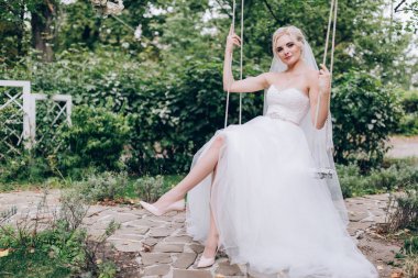 Gelin bir salıncak üzerinde beyaz elbiseli.