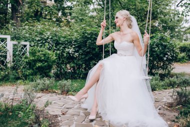 Gelin bir salıncak üzerinde beyaz elbiseli.