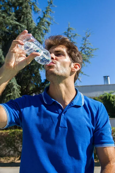 Professionell tennisspelare som bär en blå polo vilar tennis match dricksvatten från en flaska. — Stockfoto
