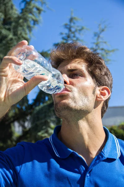 Jogador de tênis profissional vestindo um pólo azul está descansando tênis jogo beber água de uma garrafa . — Fotografia de Stock