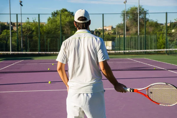 Jugador de tenis profesional jugando el juego en la cancha de tenis. Tiene la espalda a la cámara y la raqueta en la mano derecha. . — Foto de Stock