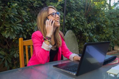 Bilgisayarla çalışırken cep telefonu üzerinde konuşurken genç girişimci kız.  