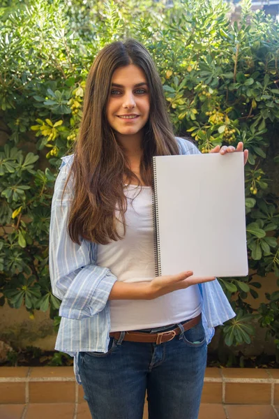 Chica emprendedora bastante blanca con ojos azules sosteniendo un cuaderno en blanco con sus manos donde se puede adjuntar un texto, un contorno o una imagen . — Foto de Stock