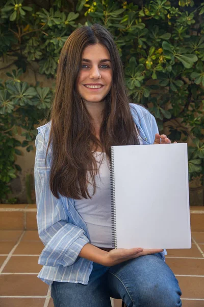 Chica emprendedora bastante blanca con ojos azules sosteniendo un cuaderno en blanco con sus manos donde se puede adjuntar un texto, un contorno o una imagen . — Foto de Stock