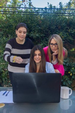 Genç Girişimciler ile bir dizüstü bilgisayar çalışma. Onlar onların şirket oluşturan üç güzel beyaz kız vardır. Onlar evlerinin terasında iş.