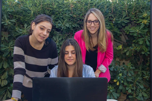Jóvenes emprendedores trabajando con un portátil. Son tres hermosas chicas caucásicas que están creando su compañía. Trabajan en la terraza de su casa . — Foto de Stock