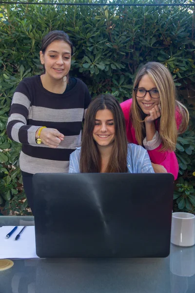 Jóvenes emprendedores trabajando con un portátil. Son tres hermosas chicas caucásicas que están creando su compañía. Trabajan en la terraza de su casa . — Foto de Stock