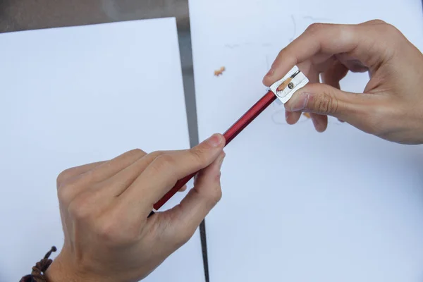 Photo of close up of a hands pulling a pencil point to continue writing on a table.